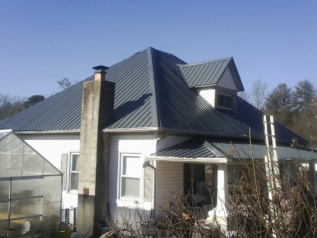 Dark blue standing seam metal roof on a white farmhouse with dormer — Slate & Tile Roof Repair by Roofing Brothers in Saint Regis