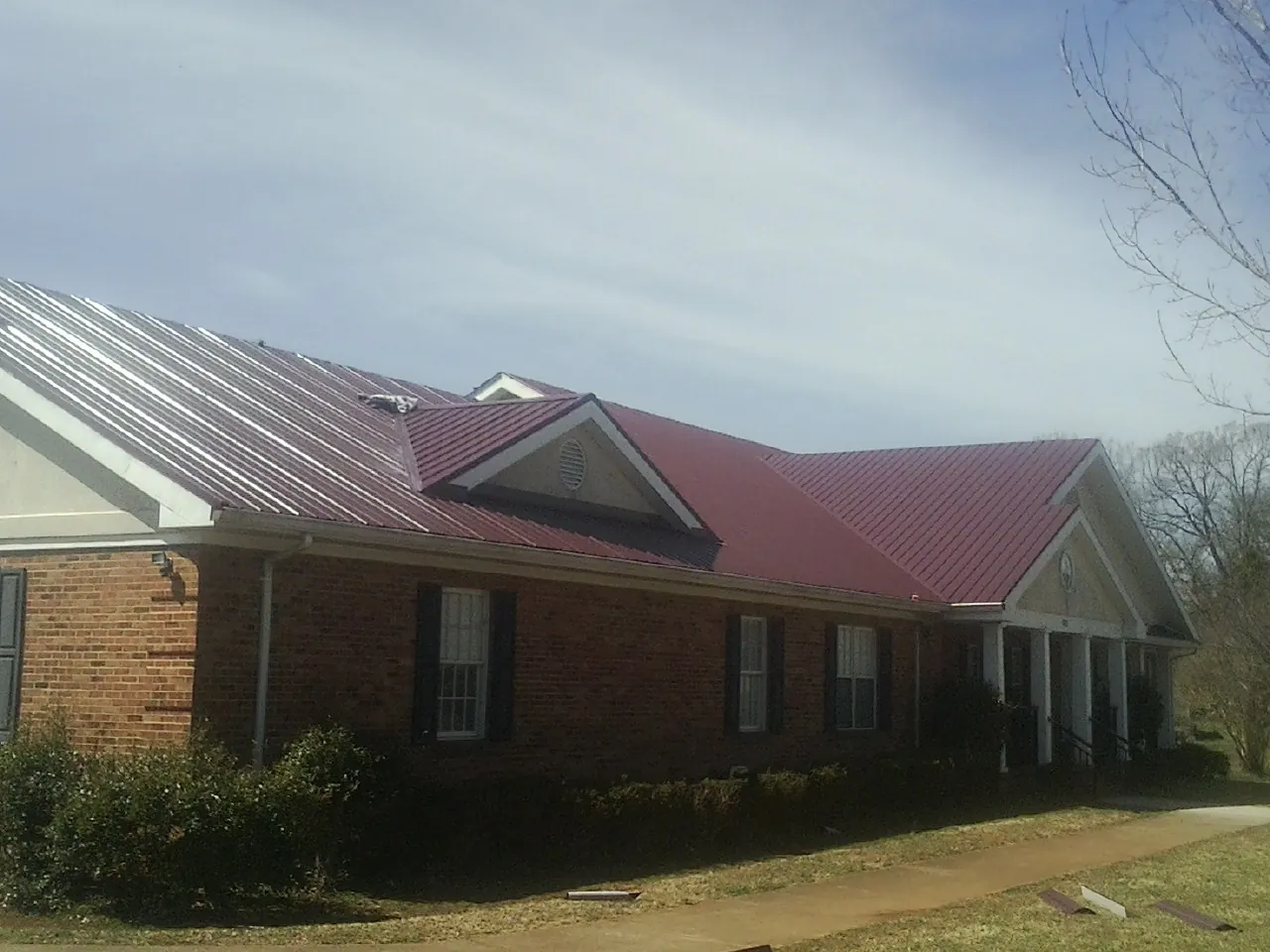 Red metal roof with gabled entries on a long brick building, from a Hail Damage Roof Repair job in Saint Regis