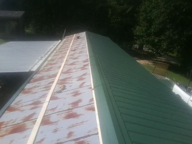 Old rusted panels beside newly installed green metal roofing — Wind Damage Roof Repair by Roofing Brothers in Saint Regis