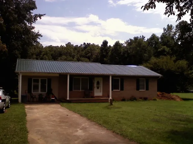 Dark green metal roof on a brick ranch with a covered porch in Saint Regis