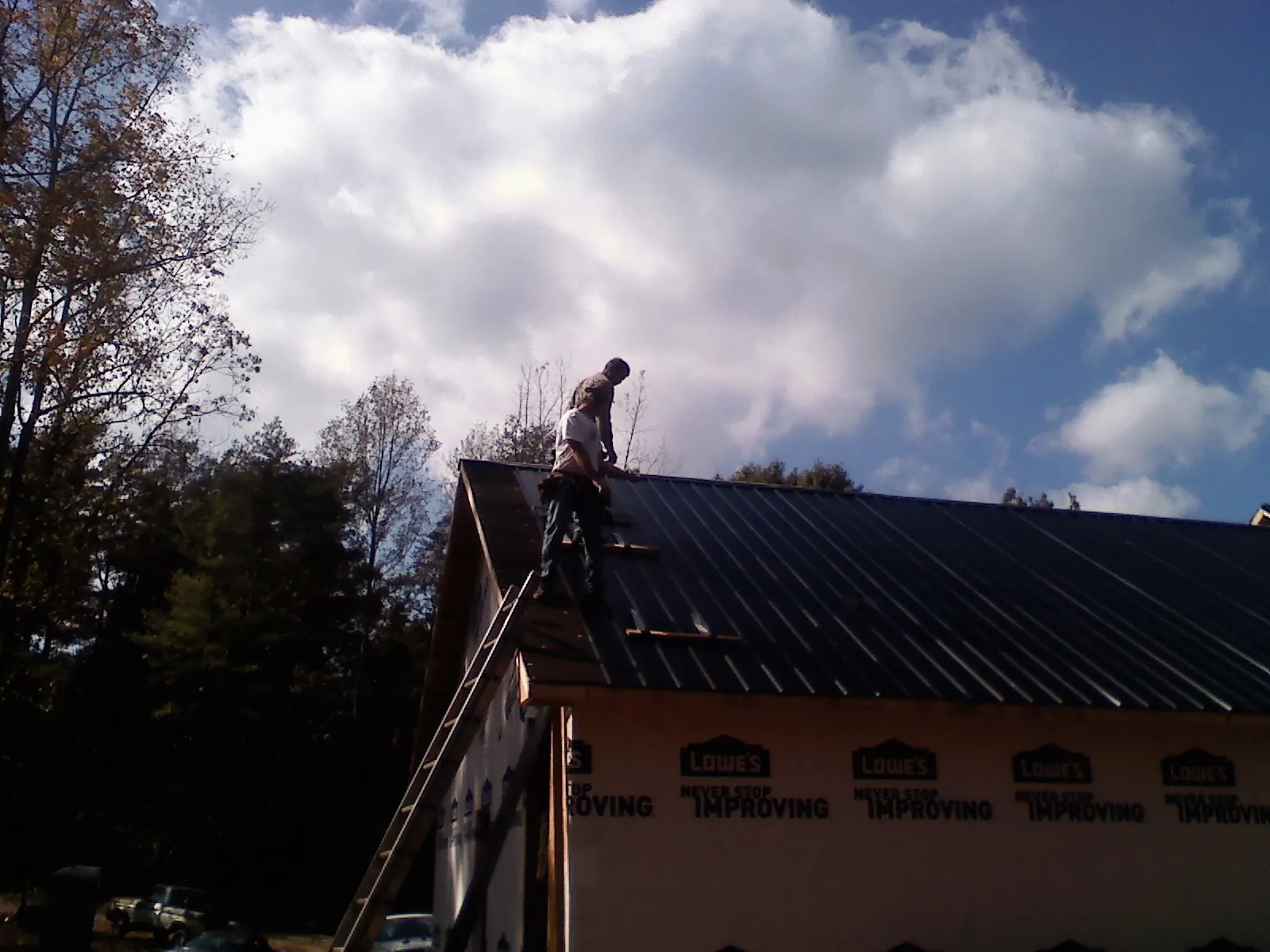 Roofer fastening dark metal panels high against a cloudy sky, from a Roof Inspection job in Saint Regis
