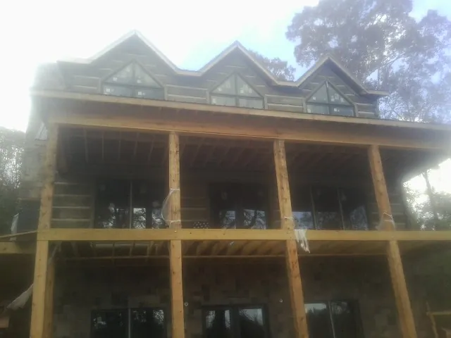 Dormers and porch framing on a large log home under construction — Roof Coating work by our crew in Saint Regis