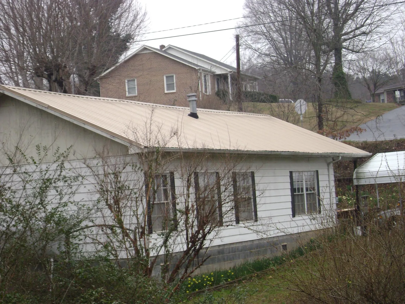 Tan metal roof on a white sided house set into a hillside — Commercial Roofing by Roofing Brothers in Saint Regis