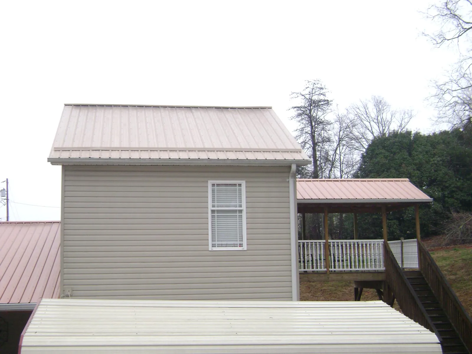 Tan metal roofs on a two story addition and attached porch, from a Roof Replacement job in Saint Regis